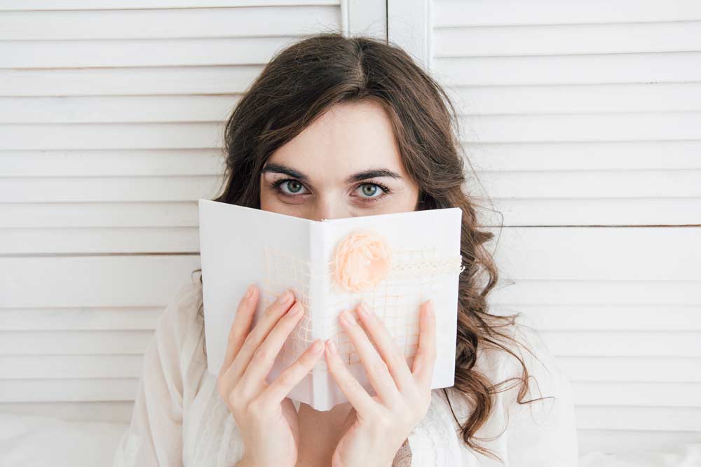 Girl writes in a five year journal notebook in bed.